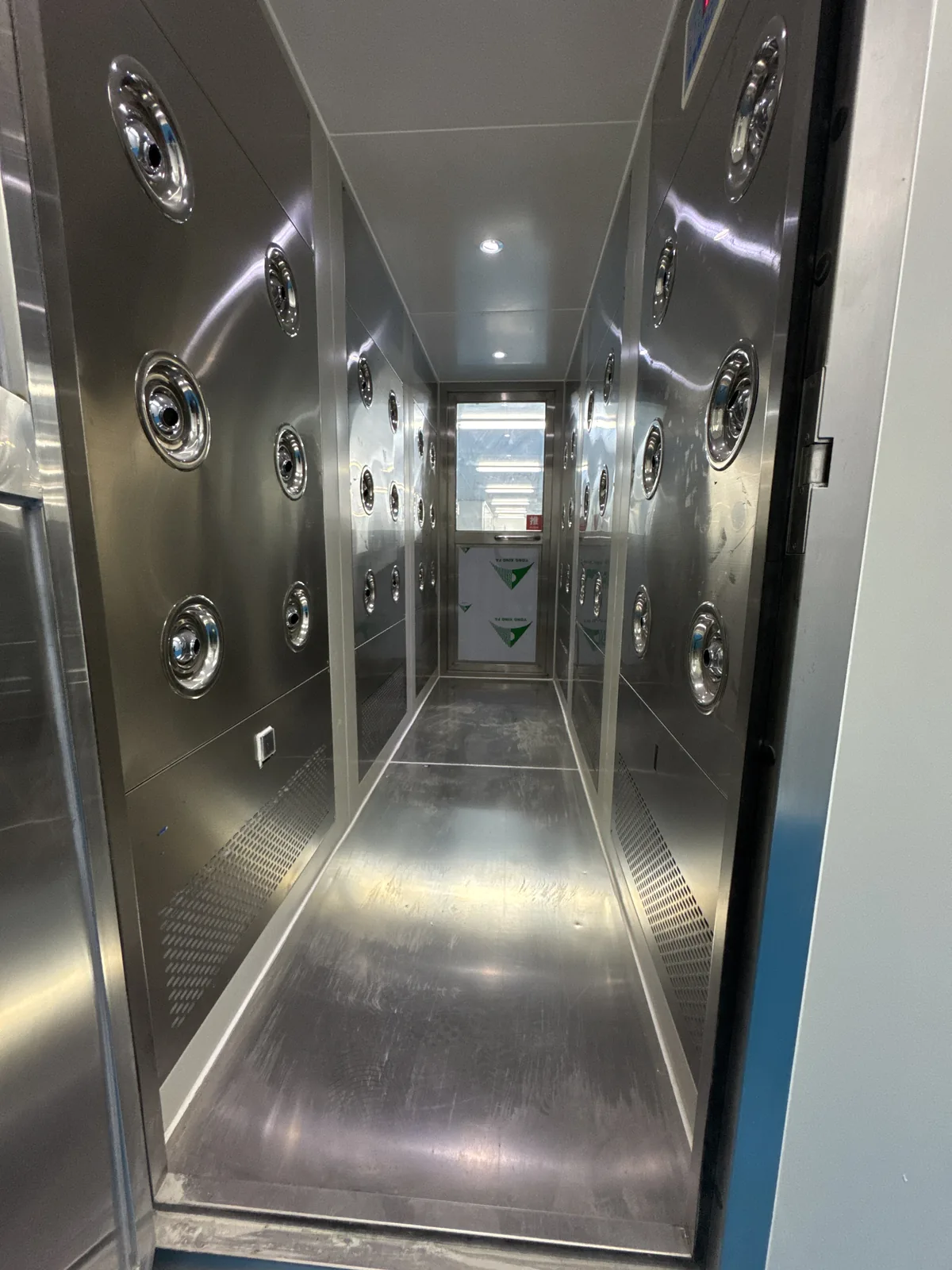 Interior of a stainless-steel air-shower passage that gives access to the controlled production area, with nozzle arrays set into the ceiling and side walls