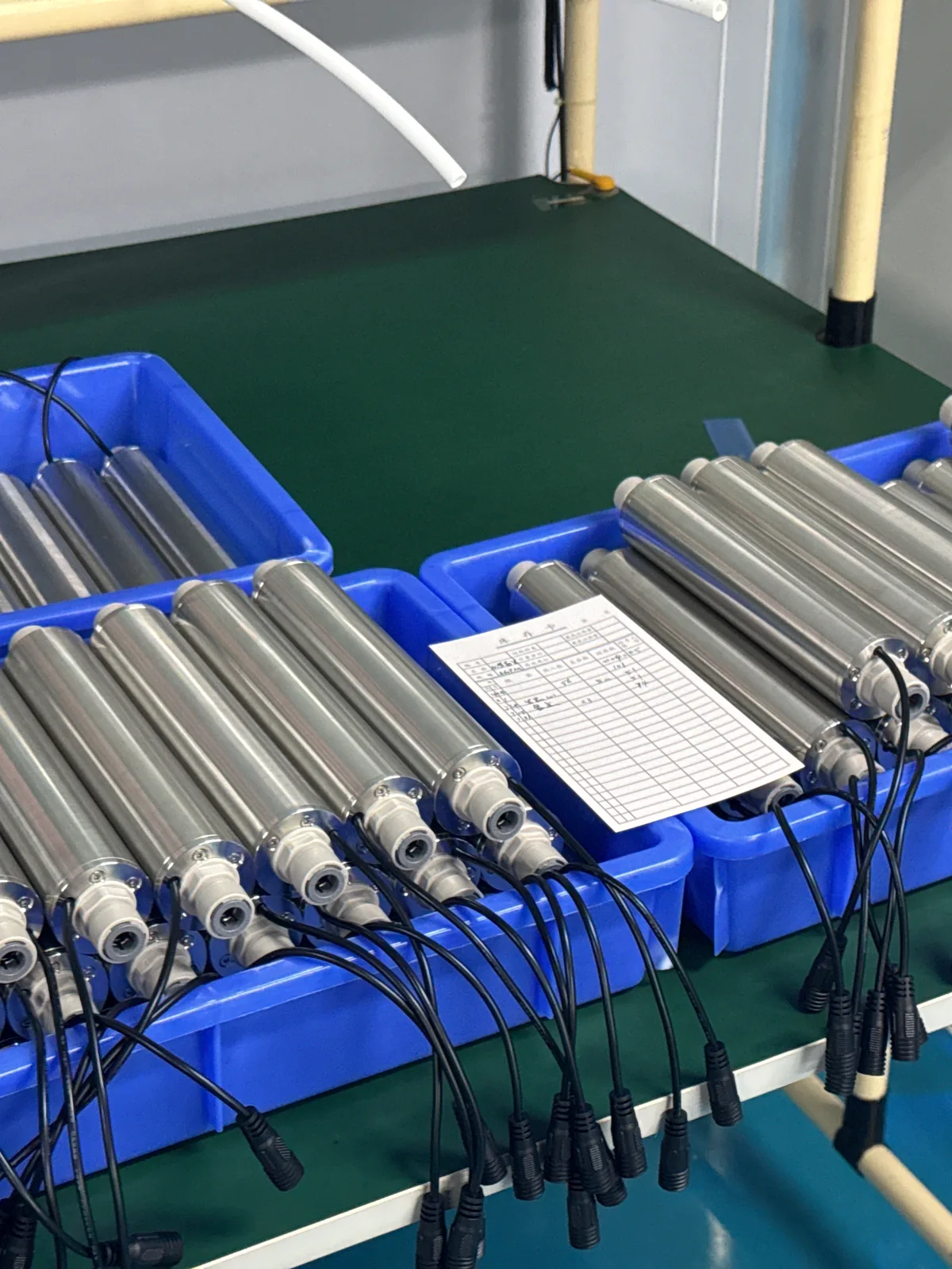 Stainless-steel UVC sterilizer housings staged in production trays, each fitted with a sealed cable gland and lead